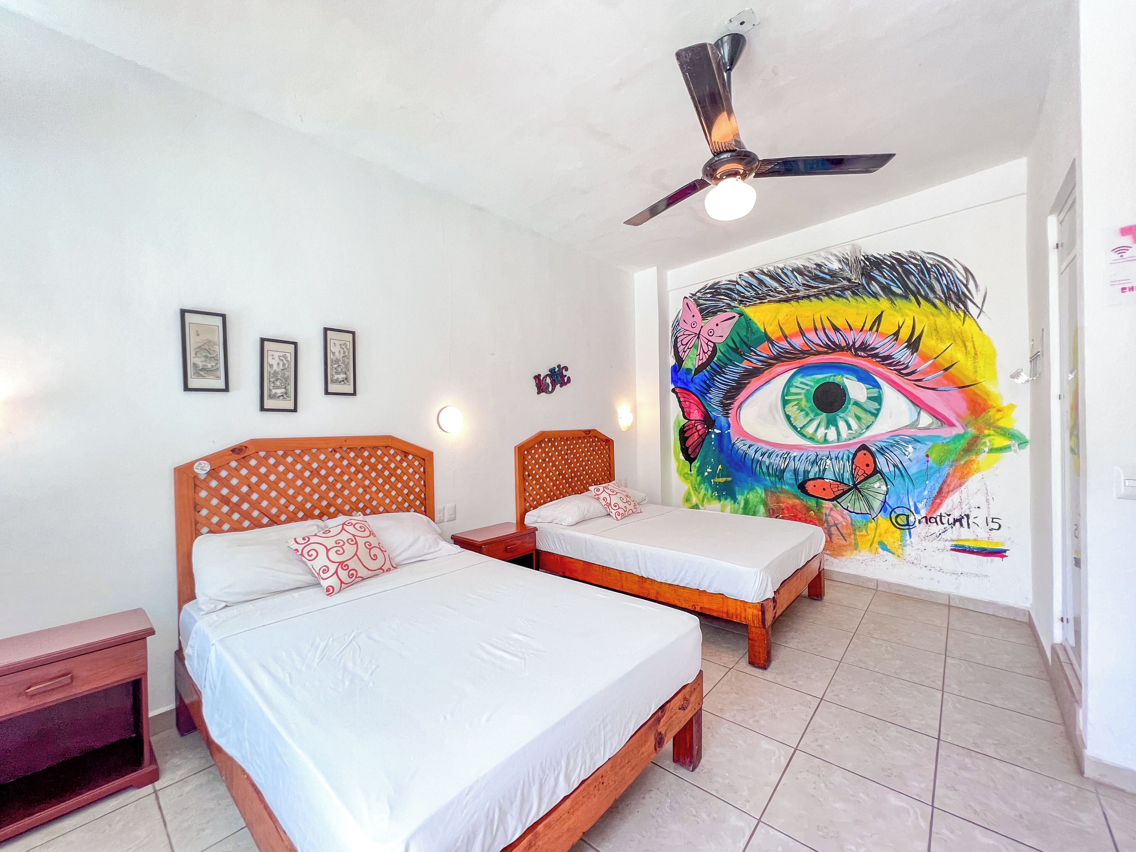 A room with two wooden beds, a ceiling fan, and a colorful mural on the wall.