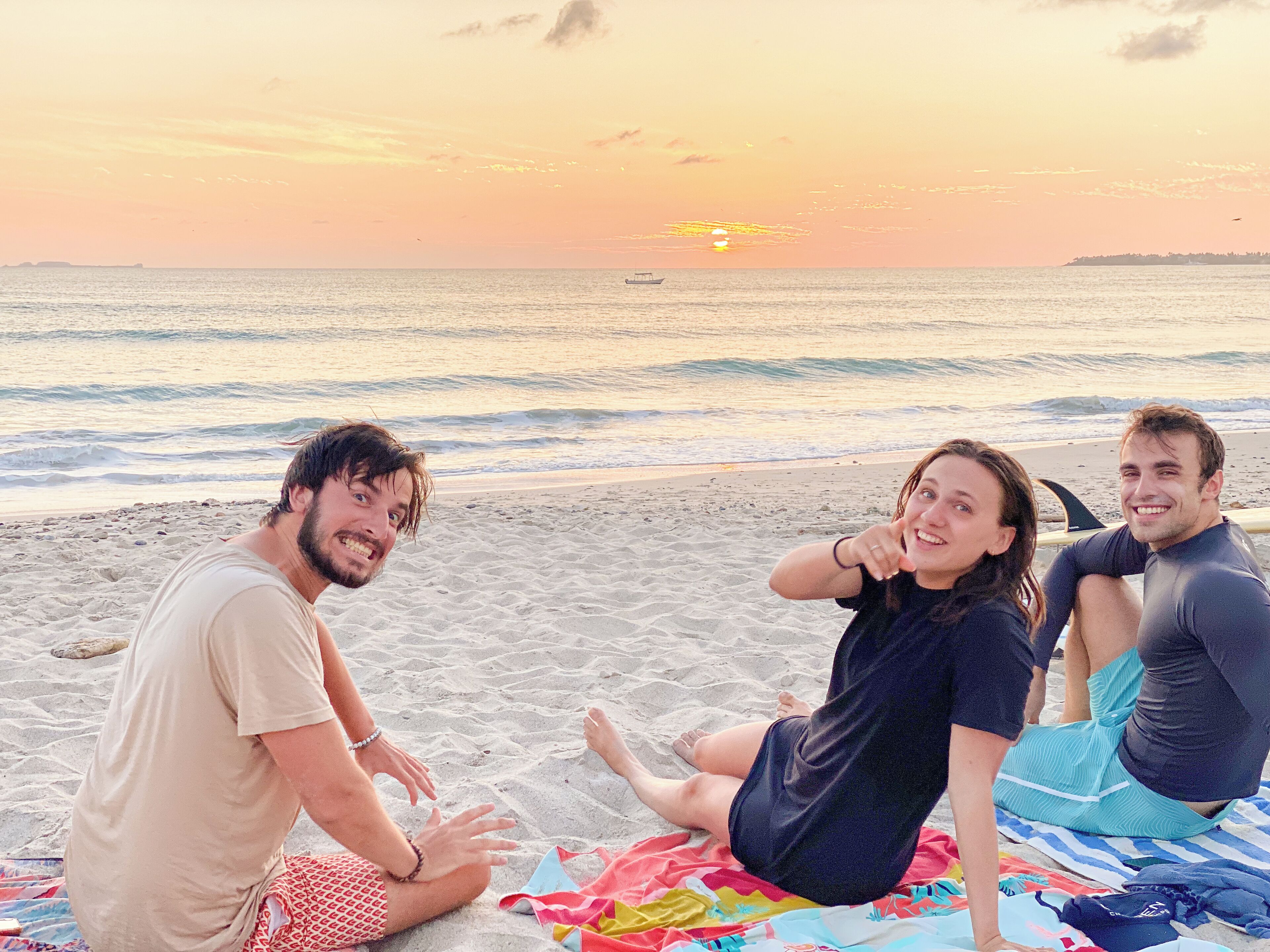 Three people sitting on a beach with a sunset in the background.