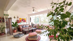 Una sala de estar acogedora con un sofá marrón, una mesa de centro y un ventilador de techo. Hay plantas en macetas y una guitarra en la pared.