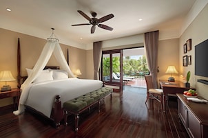 A hotel room with a large bed, a ceiling fan, a bench, a desk with a lamp, and a view of the outdoors.