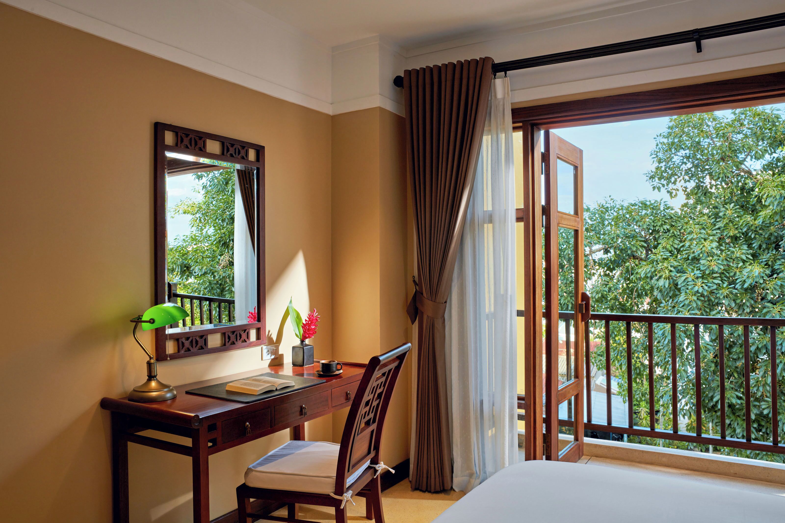 A hotel room with a desk, chair, and a large window with curtains.