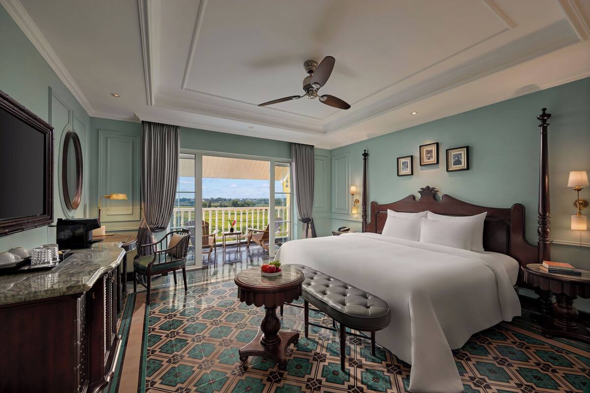 Habitación de hotel con una cama grande, un escritorio con silla, una mesita y un balcón con vistas.