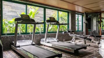 A gym with treadmills, weight machines, and a view of greenery through large windows.