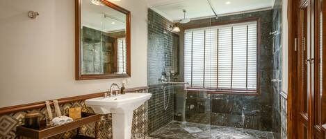 Un baño con un espejo grande, un lavabo, un mueble de tocador con toallas, una ducha con puerta de cristal y baldosas de suelo estampadas.