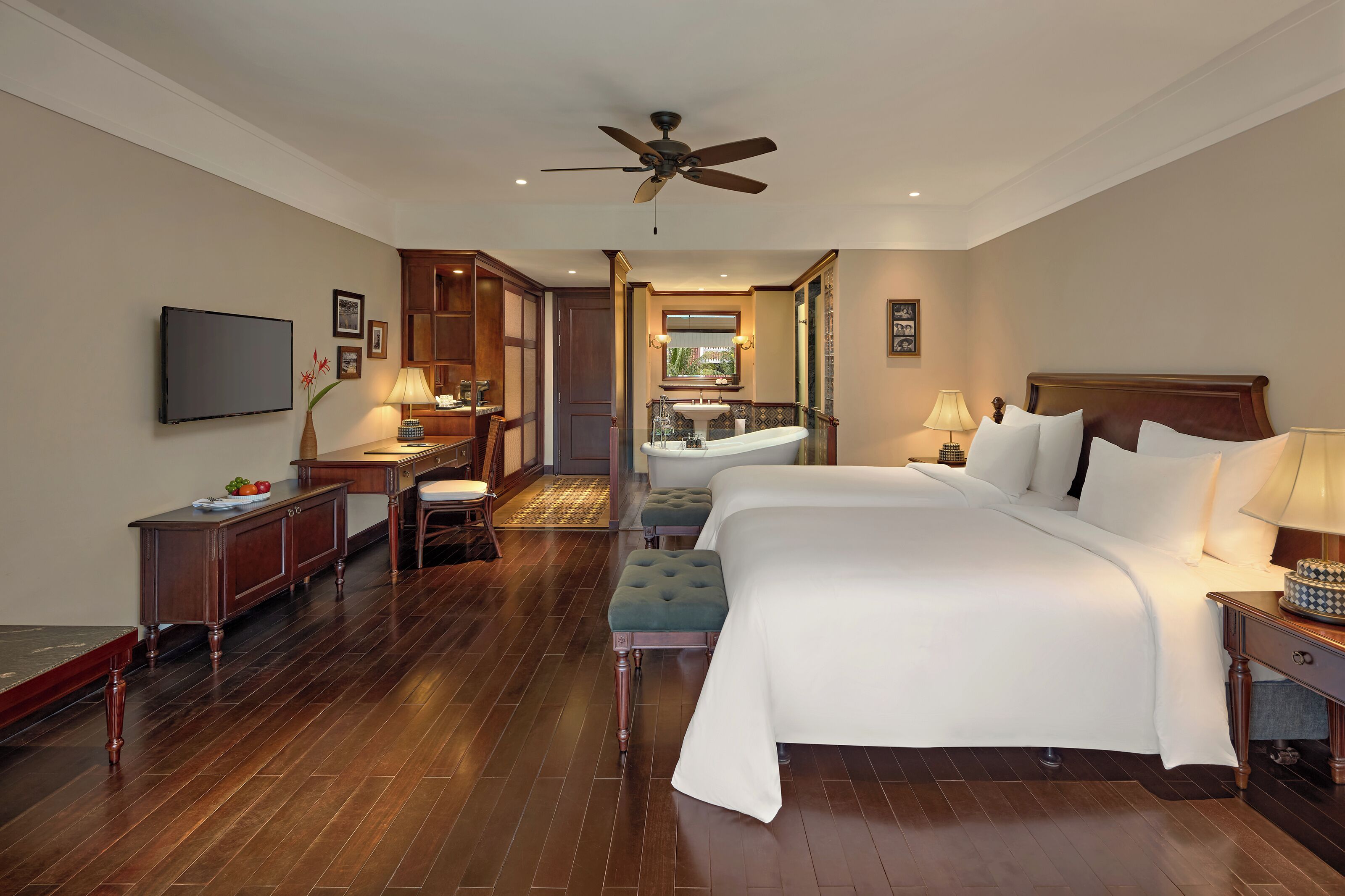 A hotel room with a large bed, a desk, a vanity with a mirror, and a ceiling fan.