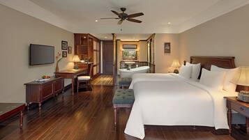 A hotel room with a large bed, a desk, a vanity with a mirror, and a ceiling fan.
