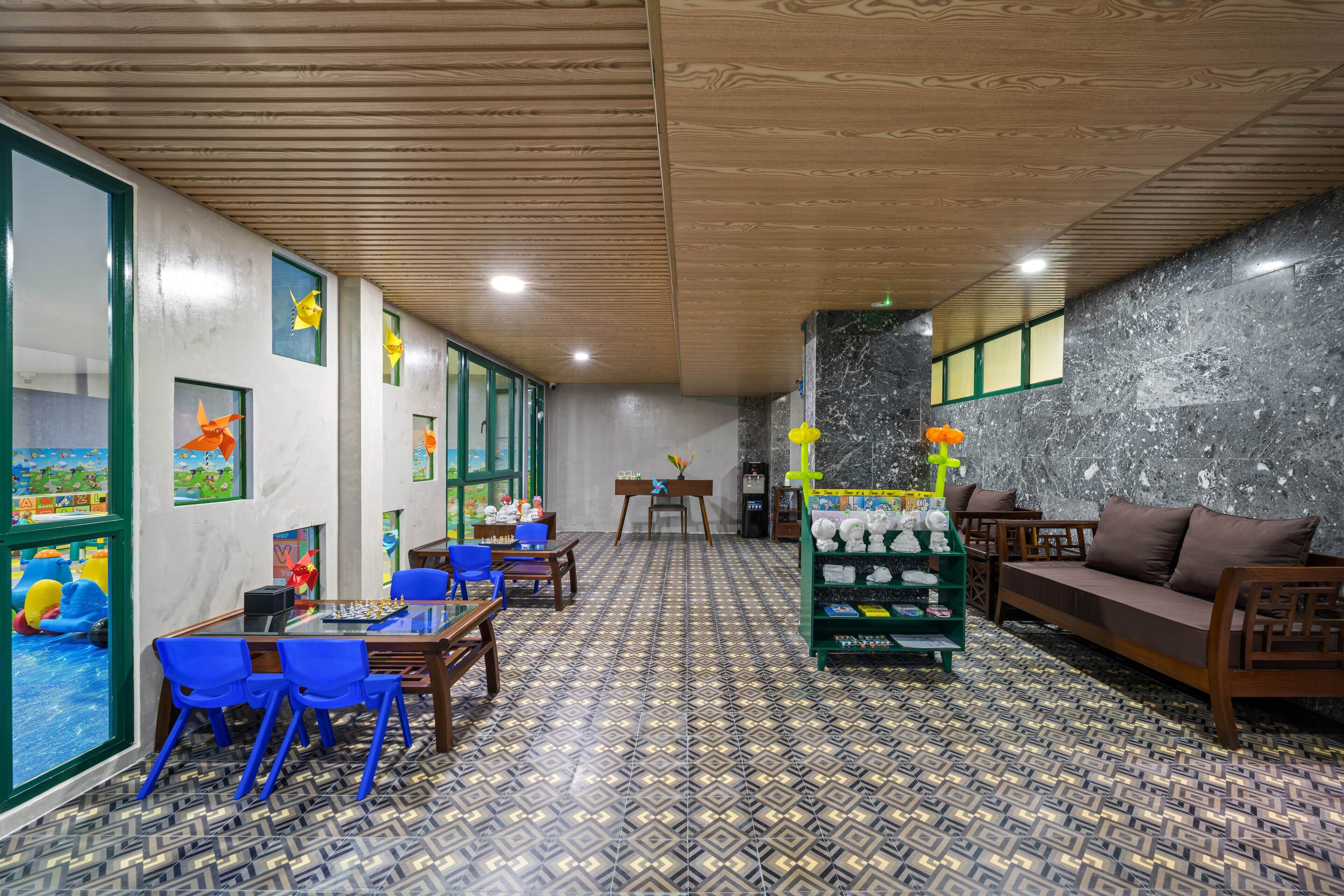 A room with a chessboard, blue chairs, a sofa, and a wall with a geometric patterned floor.