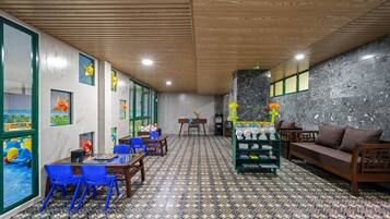 A room with a chessboard, blue chairs, a sofa, and a wall with a geometric patterned floor.