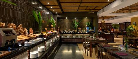 Uma área de buffet com diversas opções de comida, um balcão extenso com pratos e tigelas, e um espaço de estar com mesas e cadeiras.
