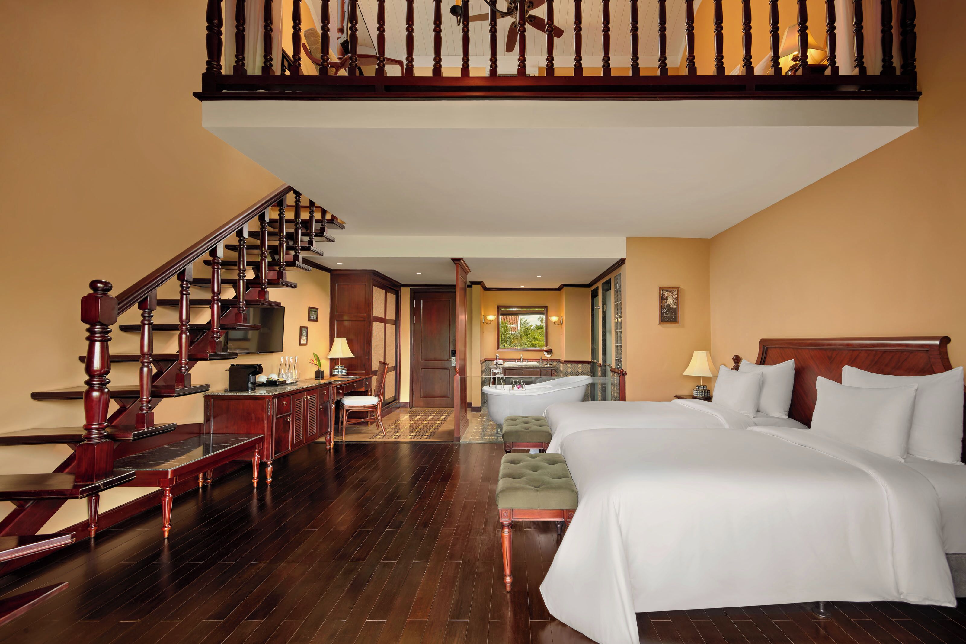 Una habitación de hotel con una cama grande, una escalera de madera, un baño con bañera y un escritorio con silla.
