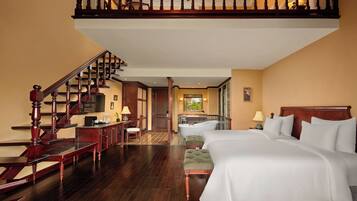 A hotel room with a large bed, a wooden staircase, a bathroom with a bathtub, and a desk with a chair.