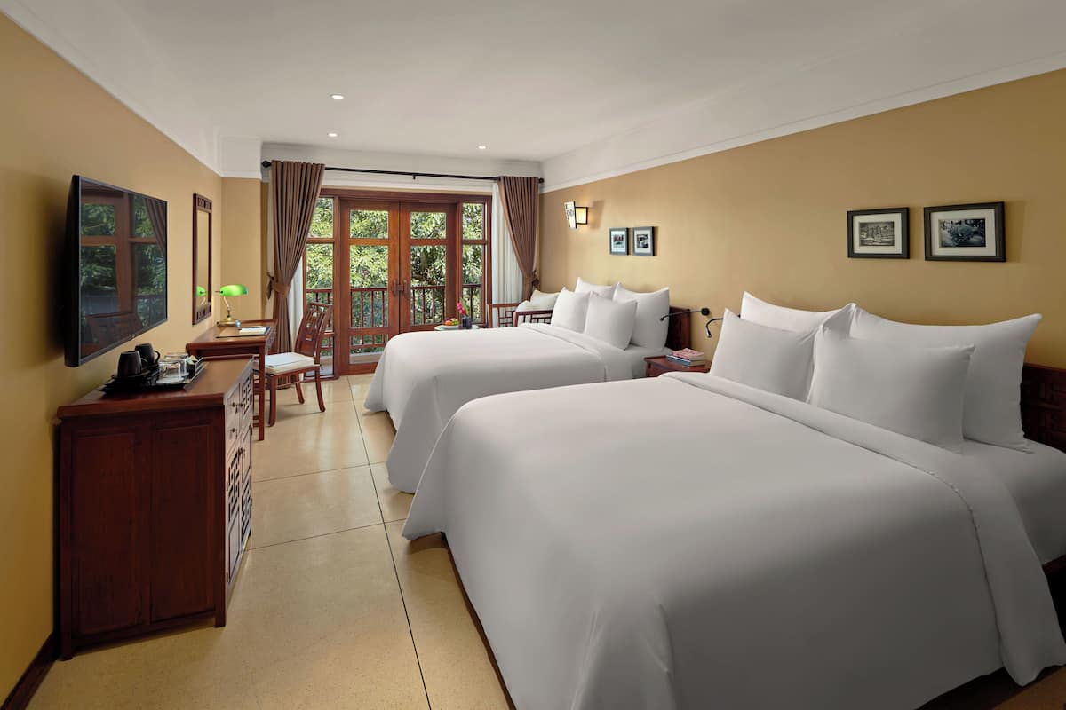 Habitación de hotel con dos camas, un escritorio con lámpara, televisión y vistas al exterior.