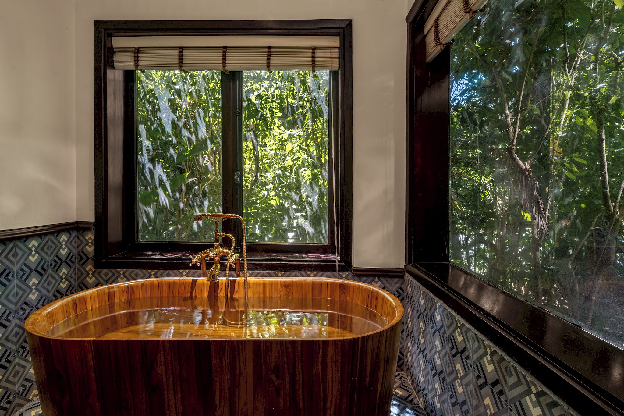 Une baignoire dont l’extérieur est en bois, une fenêtre donnant sur un paysage verdoyant et des carreaux muraux à motifs.