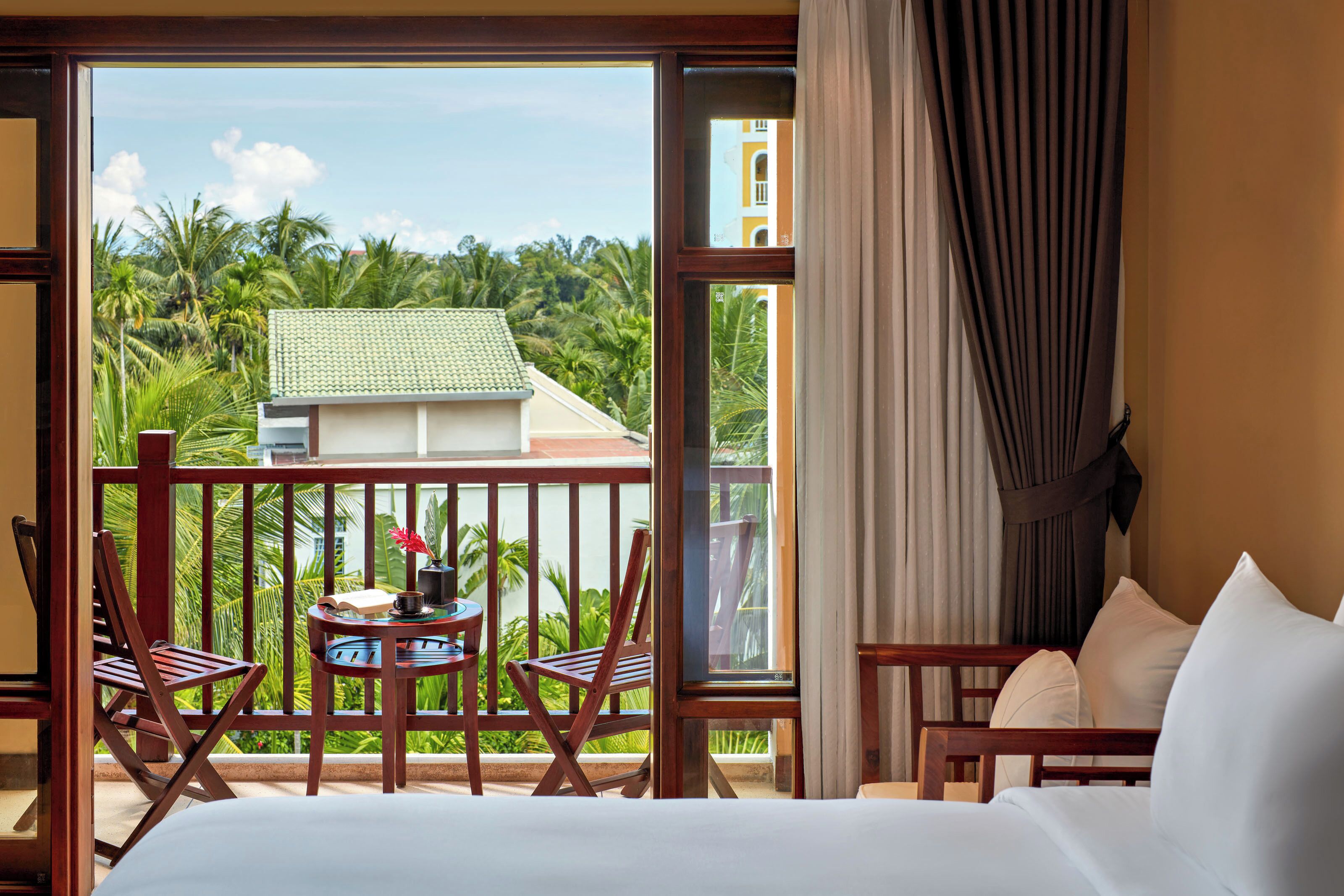 A hotel room with a balcony, a bed, a small table with a plant, and a chair.