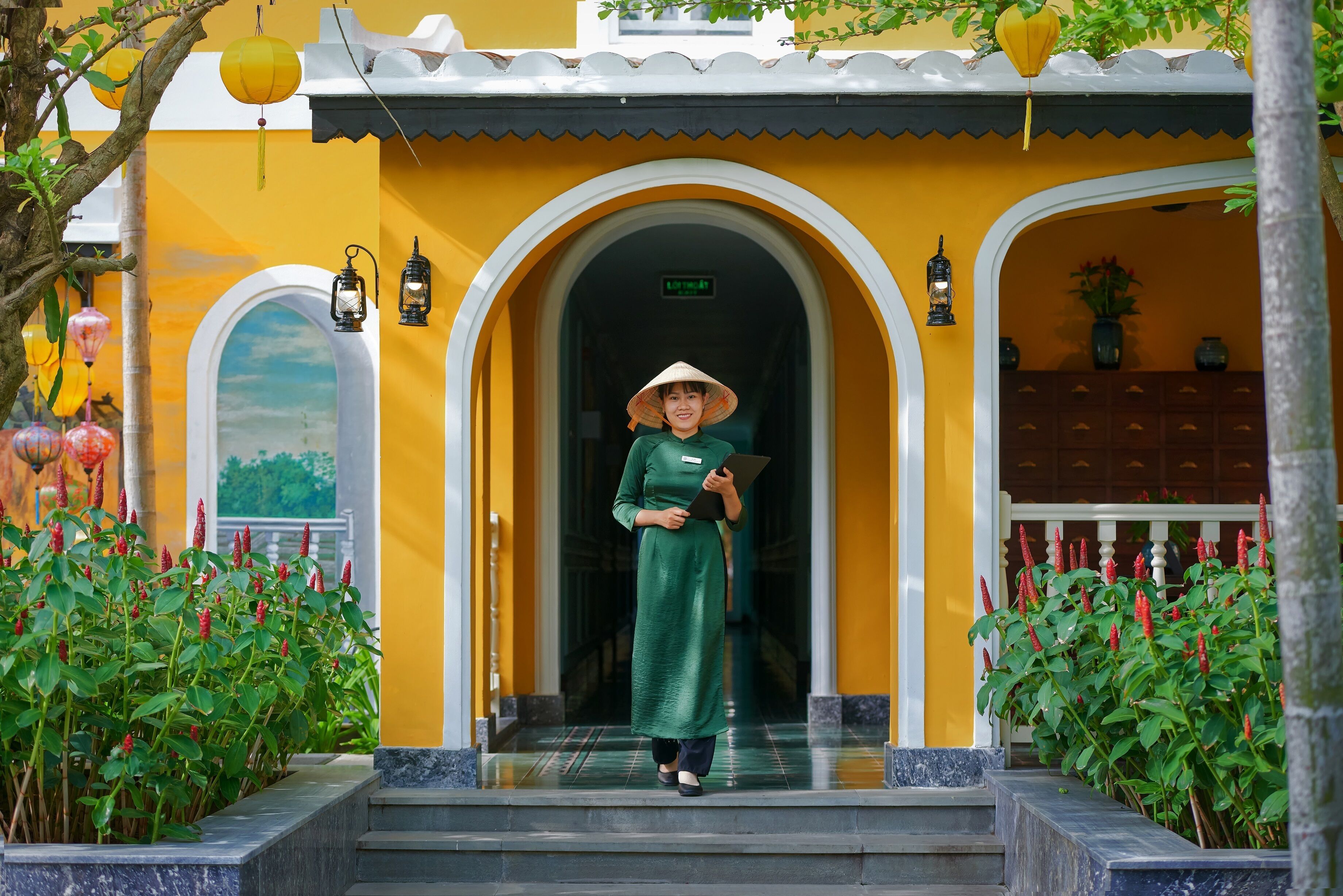 A person standing at the entrance of a building with yellow walls and a tiled roof.