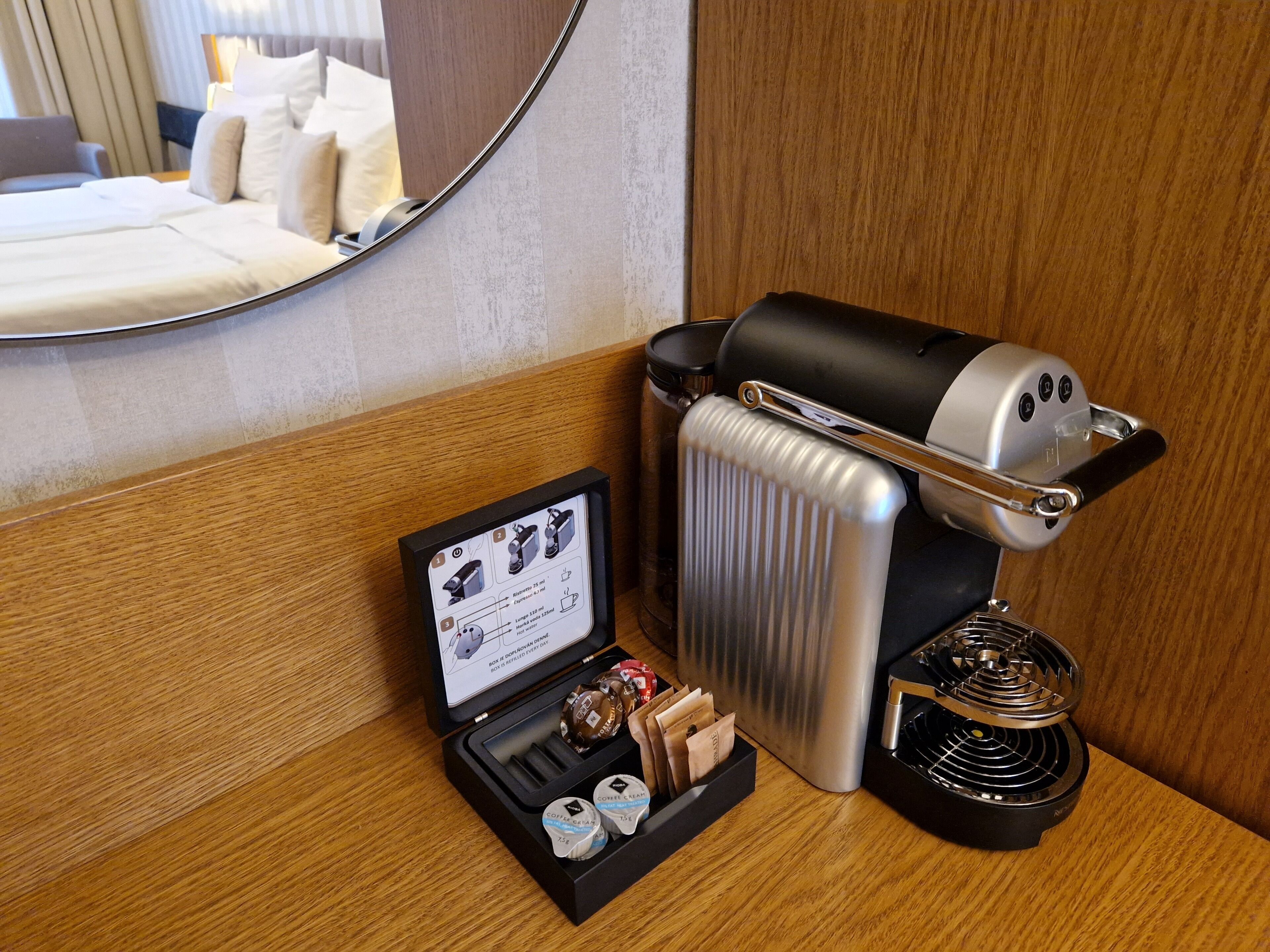 A hotel room with a coffee maker, a coffee pod holder, and a small booklet on the side table.