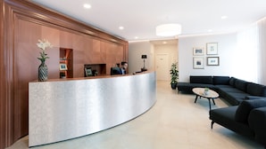 A modern reception area with a curved reception desk, a black sofa, and a small coffee table. - Hotel Schwaiger (Prague)