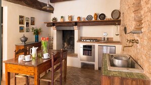 A rustic kitchen with exposed wooden beams, a stone wall, and a variety of kitchenware on shelves. - Scenic Stay in Spoleto (Spoleto)