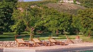 A poolside area with lounge chairs and a stone wall. - Scenic Stay in Spoleto (Spoleto)