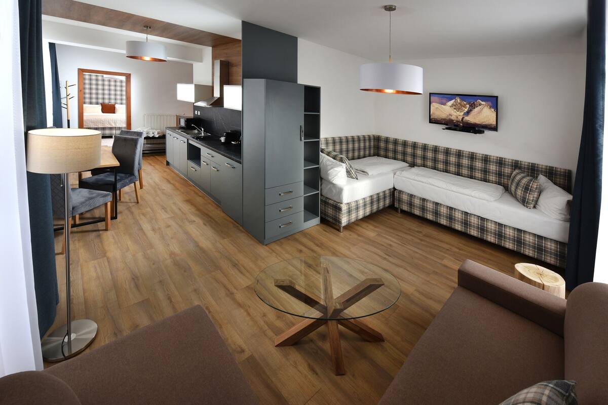 Ett modernt vardagsrum med ett soffbord i glas, en soffa, en matplats med bord och stolar samt ett köksområde.