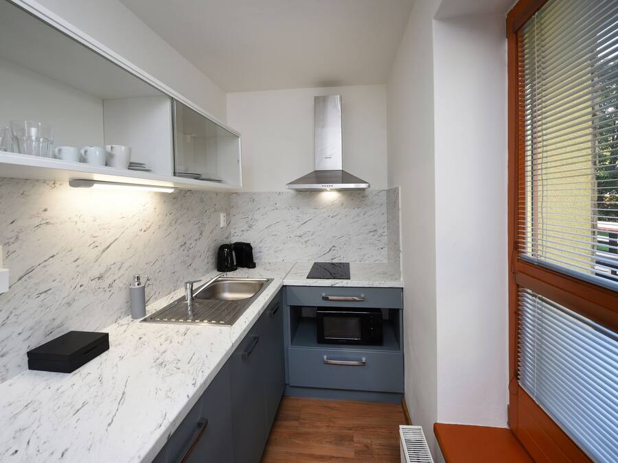 A compact kitchen with a marble countertop, a built-in oven, and a stainless steel range hood.