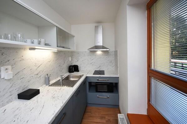 A compact kitchen with a marble countertop, a built-in oven, and a stainless steel range hood. - Aplend Vila Magnolia (Vysoké Tatry)