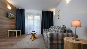 A modern living room with a wooden floor, a plaid sofa, a round wooden side table, a small round table with a glass top, and a lamp.