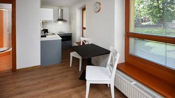 Een kleine keuken met een eethoek, een klok aan de muur en een raam met zonwering.