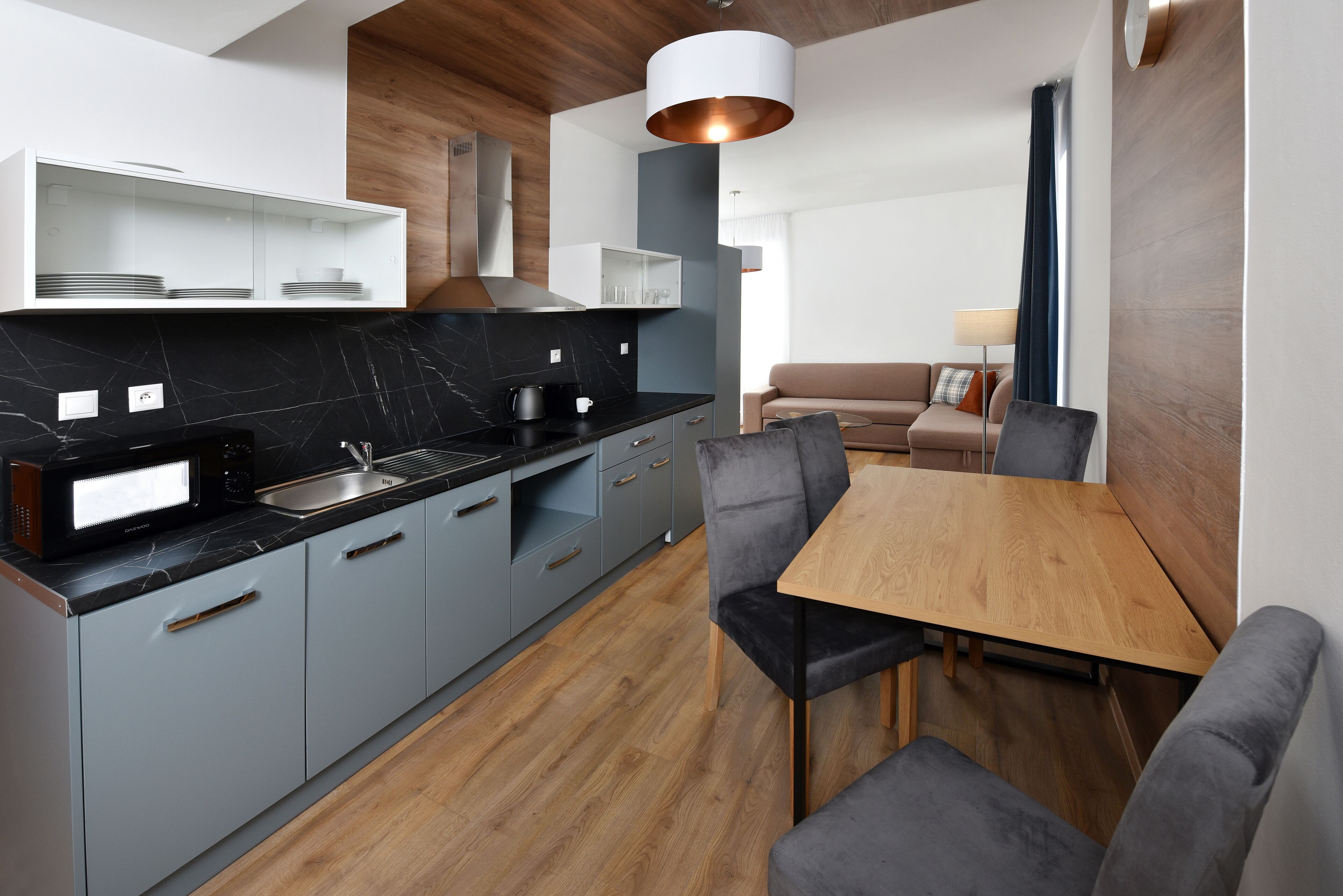 A modern kitchen with grey cabinets, a black countertop, and a wooden dining table with grey chairs.