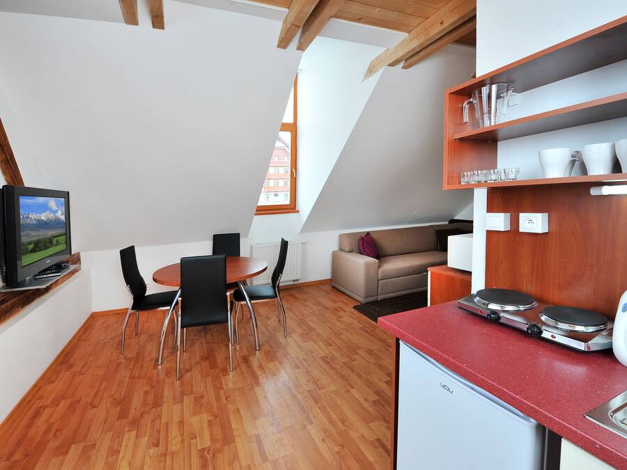 A compact kitchen with a dining area, a TV mounted on the wall, and a small refrigerator.