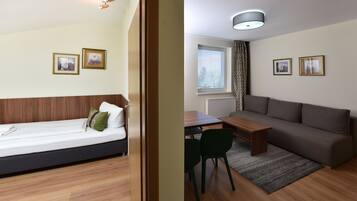 Ein Zimmer mit einem Bett, einer Couch, einem Esstisch und zwei Stühlen. An der Wand hängen zwei gerahmte Bilder.