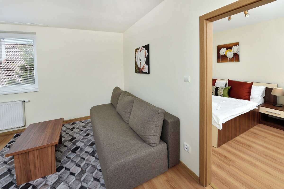 Una habitación compacta con sofá, una pequeña mesa de madera y cama con cabecero de madera.