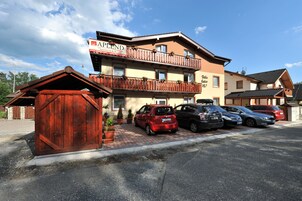 Un hotel de varios pisos con fachada de madera, balcones y un estacionamiento con varios coches.