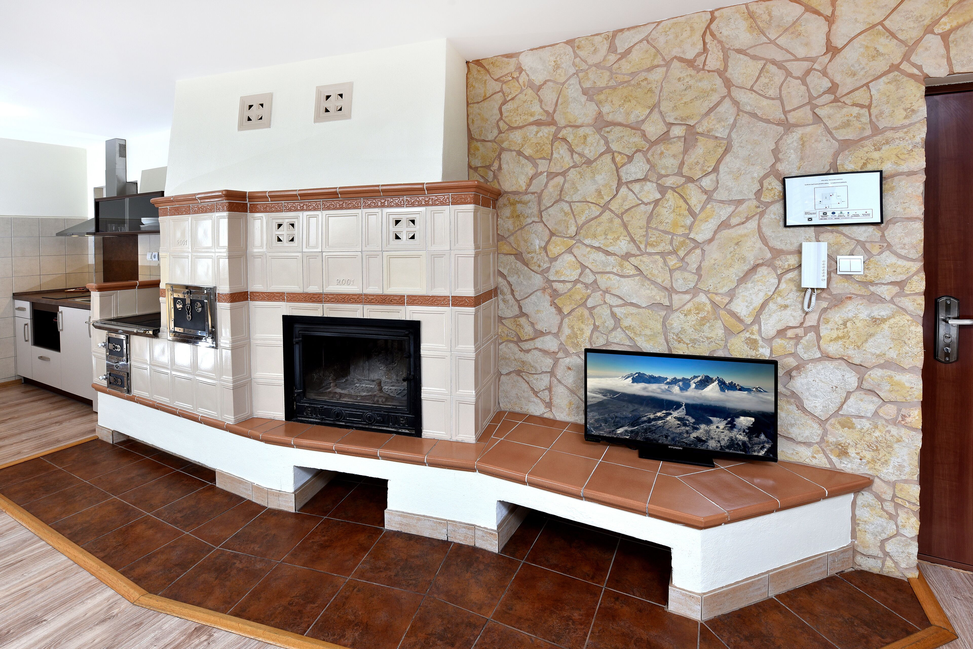 A modern kitchen with a built-in fireplace, stone wall, and a flat-screen TV mounted above it.