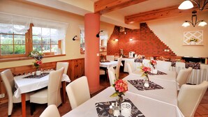 A restaurant with multiple tables, white chairs, and a brick wall. - APLEND Bed & Breakfast Júlia (Vysoké Tatry)