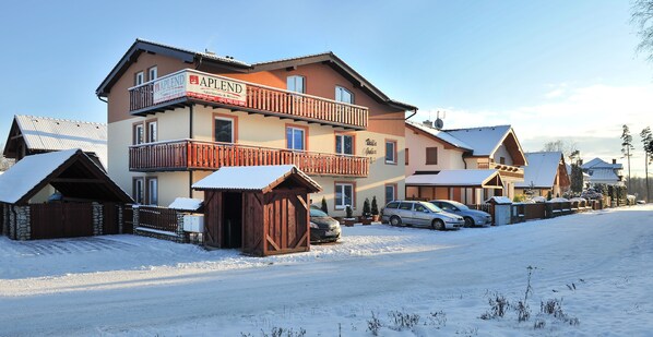 Um edifício de vários andares com varanda, paisagem coberta de neve e carros estacionados.