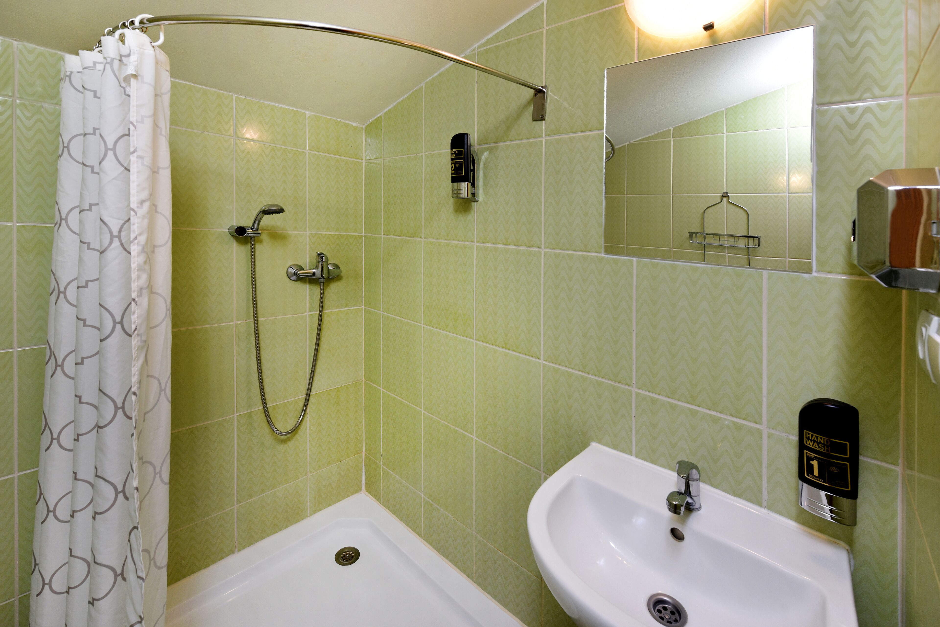A bathroom with a shower, a sink, a mirror, and a soap dispenser.