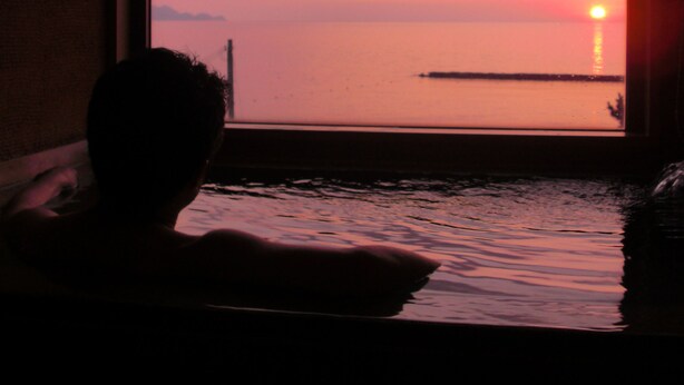 A person in a bathtub with a sunset view through a window. - Hotel Ichiboukan (Kyotango)