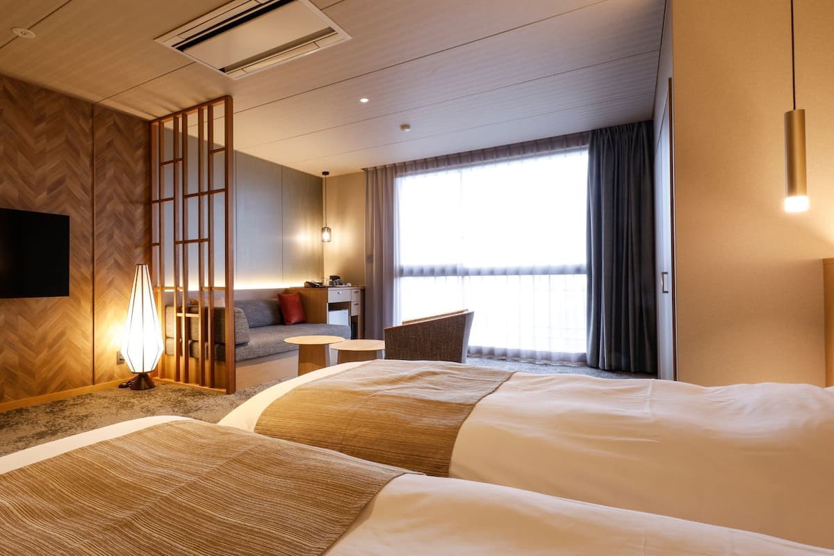 A hotel room with two beds, a TV, a desk, a sofa, and a large window.