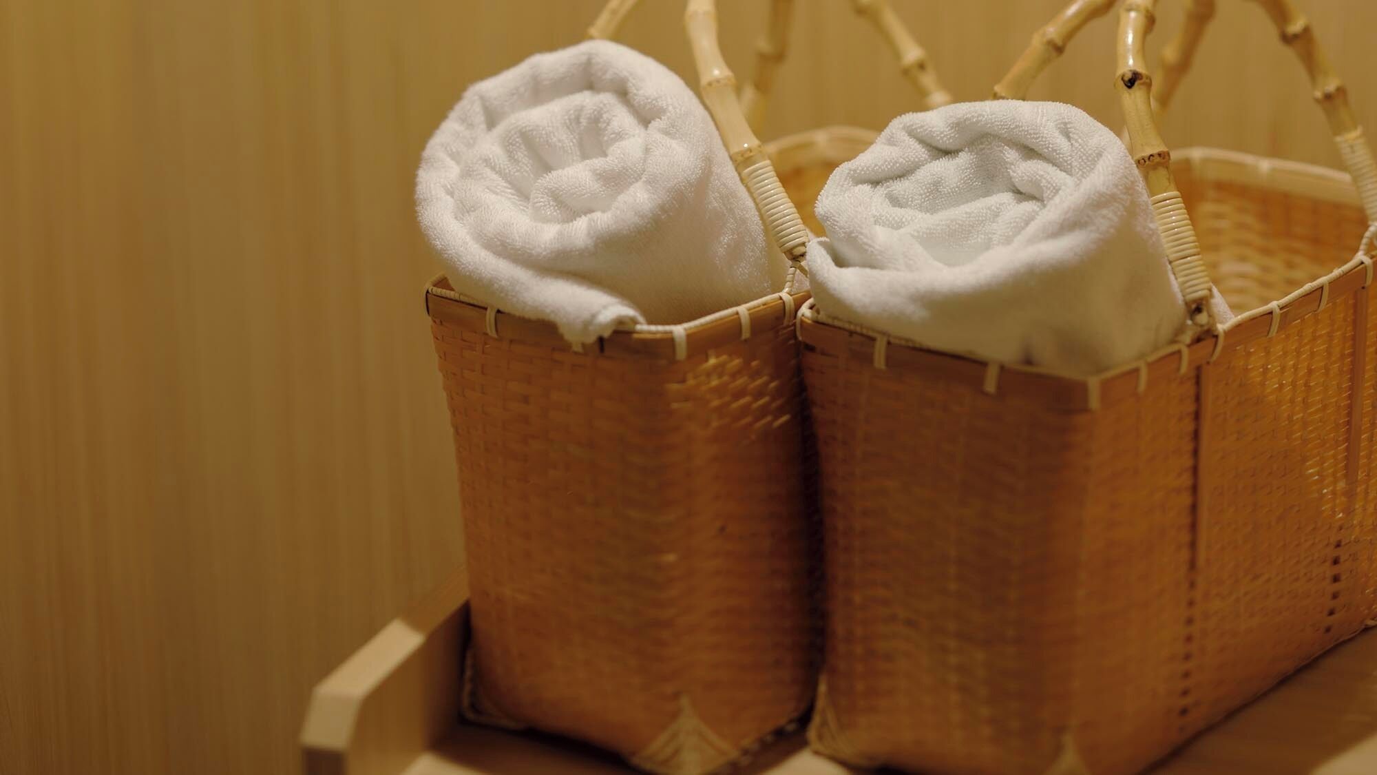 Two wicker baskets with white towels placed on a wooden surface.