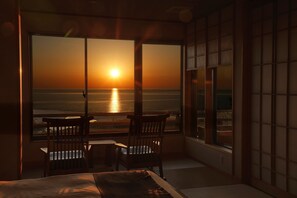 A room with a bed, two chairs, a small table, and a view of the ocean at sunset. - Yuhigaura Onsen Ryotei KAI (Kyotango)