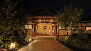A traditional Japanese building with a tiled entrance pathway, wooden gates, and a lantern.