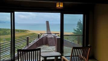A room with a large window overlooking a beach and ocean. There are two wooden chairs and a small table.