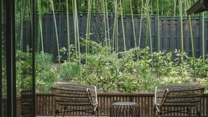 A wooden deck with two wicker chairs and a round table, surrounded by bamboo plants and a wooden fence. -  Ujo Soan (Kyotango)