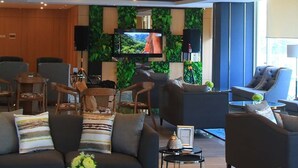 Un moderno vestíbulo de hotel con un sofá, sillones, un televisor y una pared decorada con follaje verde.