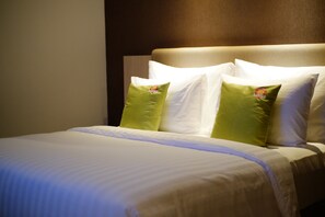 Una cama bien hecha con sábanas blancas y almohadas verdes, un cabecero y una pared lisa.