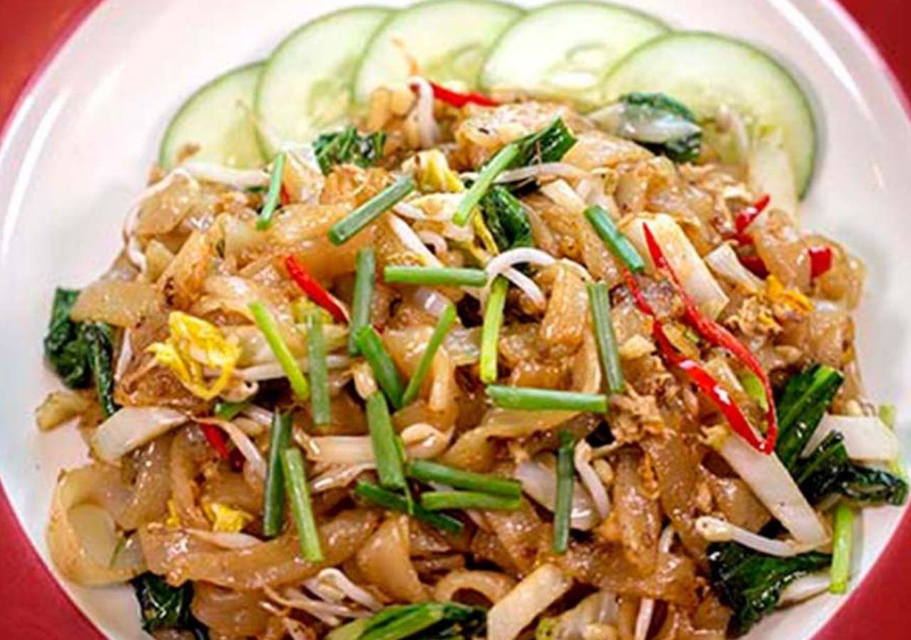 A plate of stir-fried noodles with vegetables and slices of cucumber.