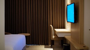 Habitación de hotel con cama, escritorio, silla, televisor y cortina.