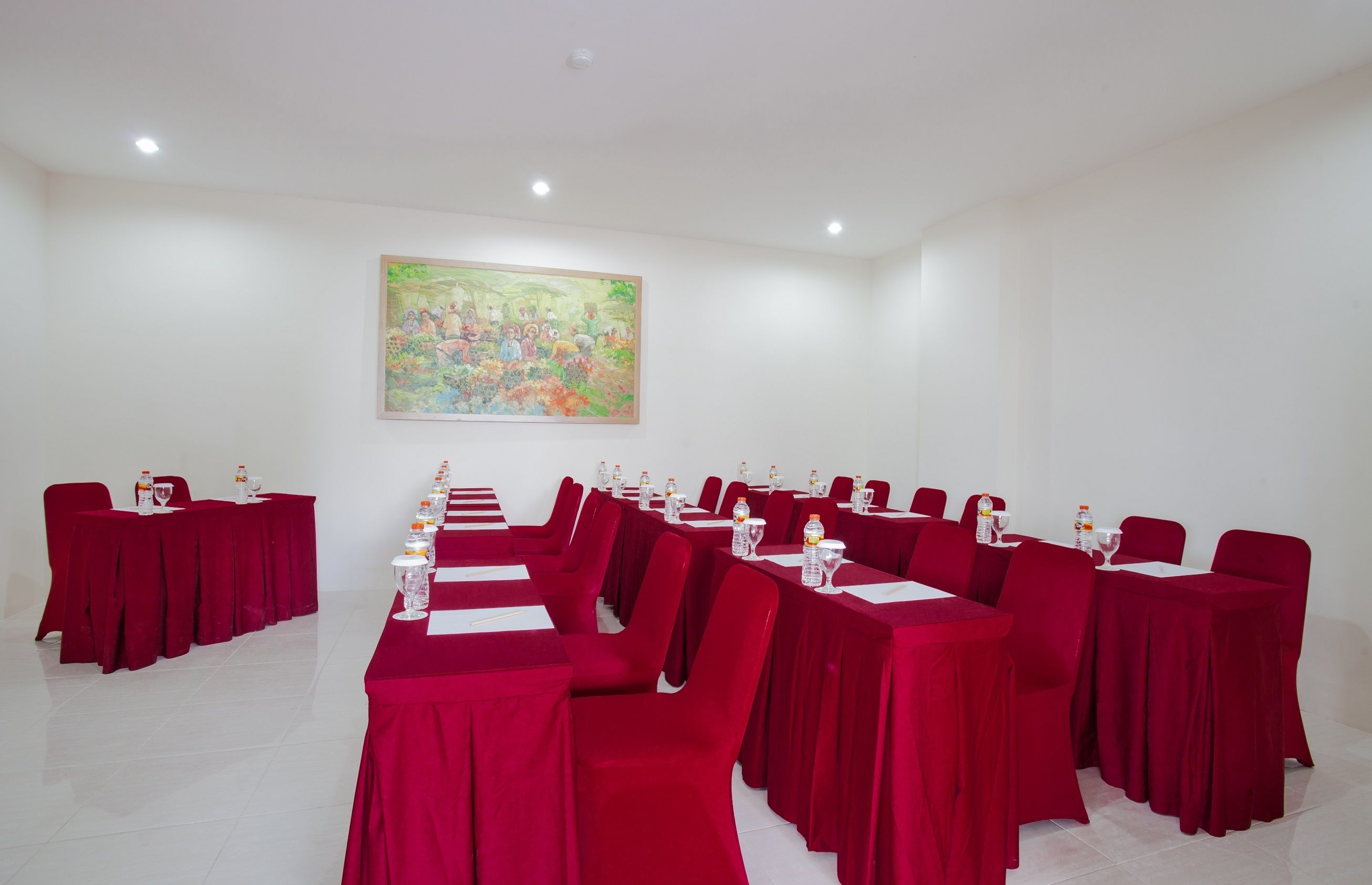 A conference room with tables set for a meeting, red chairs, and a large painting on the wall.