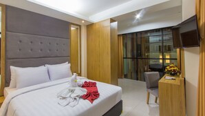 Una habitación de hotel moderna con una cama grande, cabecera de madera, televisor de pantalla plana y una pequeña mesa de trabajo con un florero.
